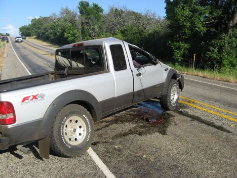 1979 Ford Bronco - A silver pickup truck with FX4 badging is parked on the side of a road, with debris scattered on the asphalt.