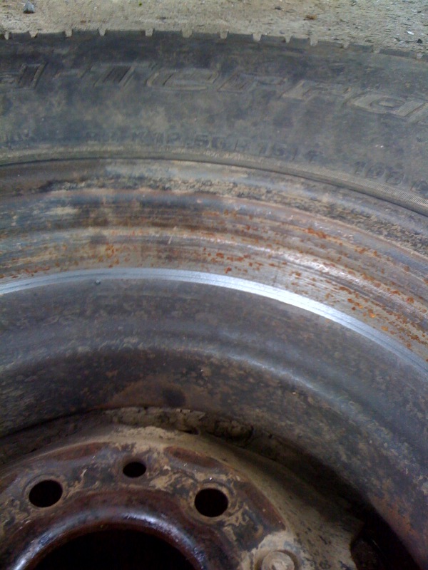 Close-up of a rusty steel wheel with a worn tire. Tire sidewall text is partially visible