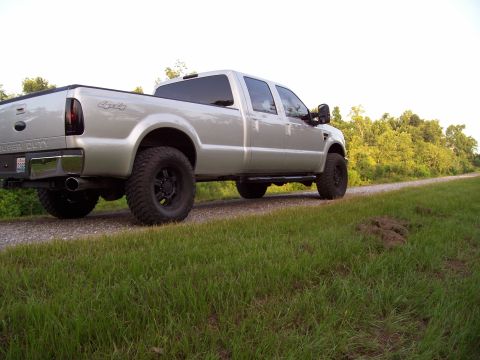 2008 Ford F-250 - A silver 2008 Ford F-250 Super Duty pickup truck is parked on a gravel road with grassy verges and trees in the background.