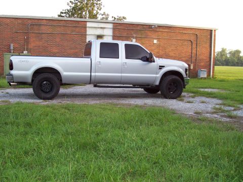 2008 Ford F-250 - A silver crew cab pickup truck is parked on a gravel lot next to a brick building.