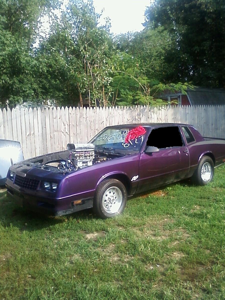 Purple 1981 Chevrolet Monte Carlo with hood open, showing a supercharger. The car has racing wheels and a red cloth on the windshield