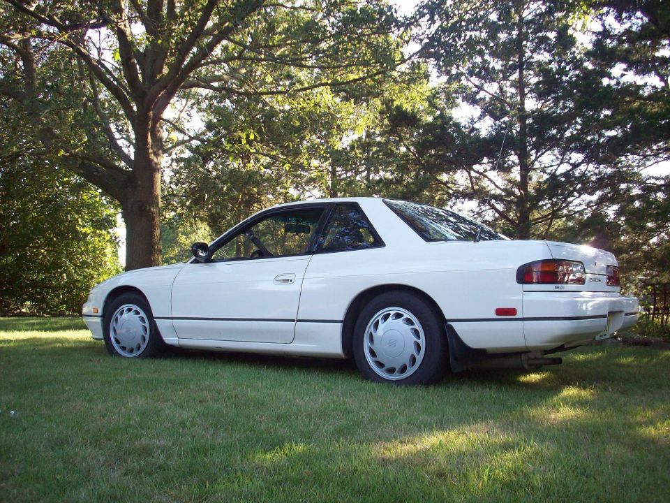 White coupe parked on grass, rear three-quarter view. Hubcaps visible