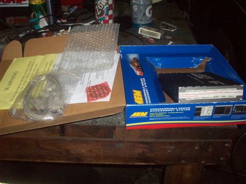 1992 Nissan 240SX - Contents of an AEM Programmable Engine Management System, including the main unit, wiring, and documentation, laid out on a wooden surface.