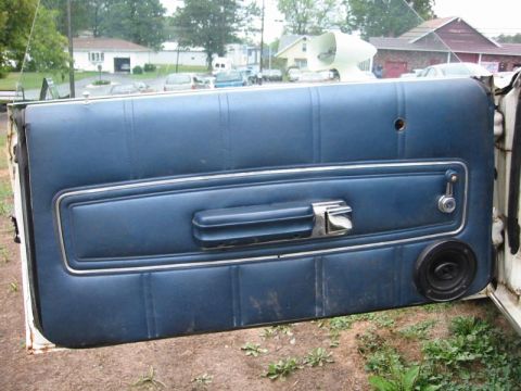 1971 Ford Ranchero - Interior view of an open driver's door on a white vehicle, showing a dirty blue vinyl door panel with a chrome-trimmed armrest/pull strap,…