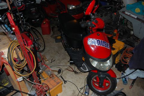 2010 Kawasaki BAYOU 220 - A red scooter with an Oilers logo is parked in a garage filled with various equipment and tools.