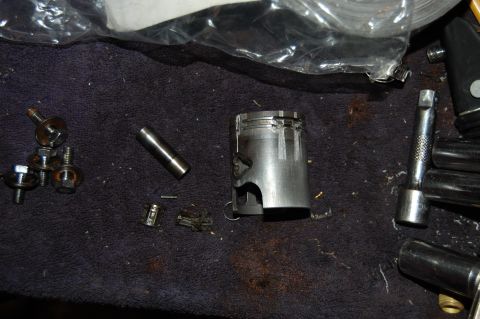 2010 Kawasaki BAYOU 220 - A damaged piston and engine components are laid out on a dark cloth, with tools nearby.
