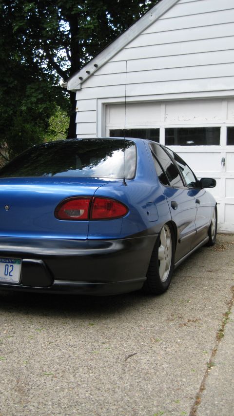 1996 Chevrolet Cavalier - The rear of a blue sedan is visible, parked on a concrete driveway in front of a white garage door.