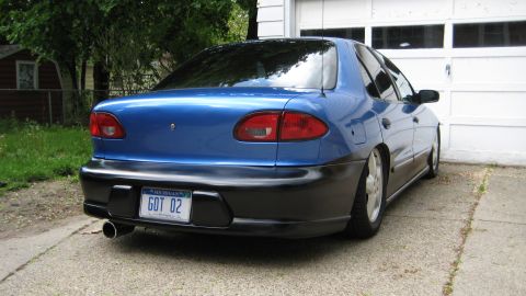 1996 Chevrolet Cavalier - Rear view of a blue sedan with custom black trim and a lowered stance parked in front of a garage door.