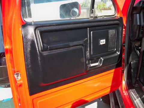 1985 Ford Bronco - Close-up of an orange vehicle's interior door panel with black trim and chrome accents.