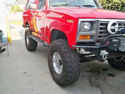 1985 Ford Bronco - This red Ford Bronco features off-road tires and a winch, suggesting it's built for terrain.