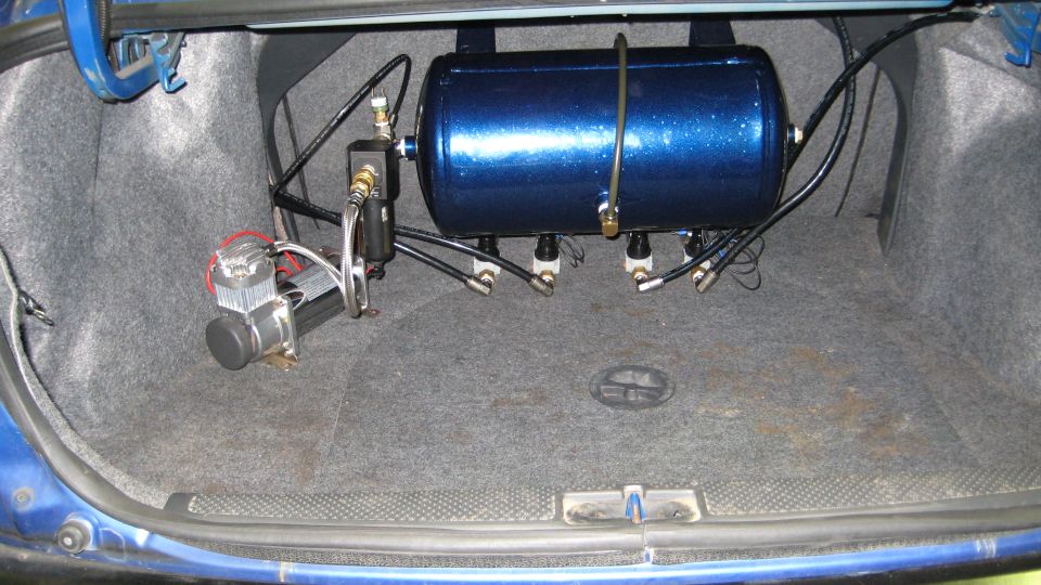 Blue air tank, four solenoid valves and chrome compressor mounted in a car trunk