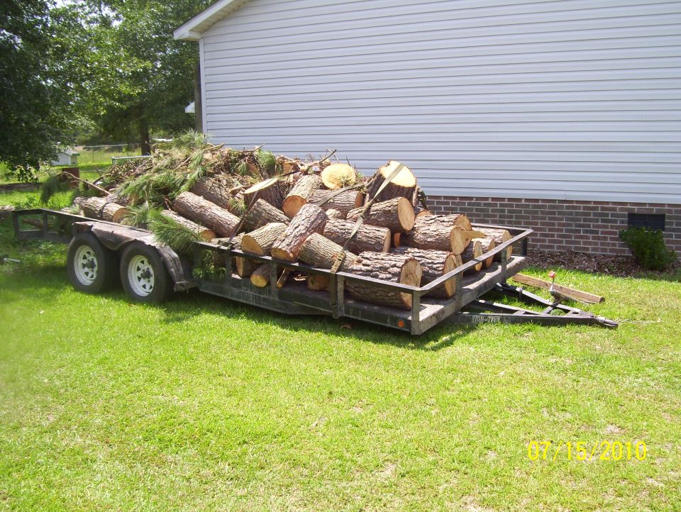 Trailer loaded with logs parked on grass, house in background. Watermark reads 07/16/2010 SUPERMOTORS.NET