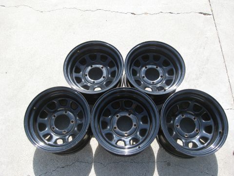 1986 Ford Bronco - A set of five black steel wheels, likely aftermarket, are displayed on a concrete surface.