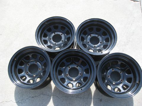 1986 Ford Bronco - Set of five black steel wheels, likely aftermarket, displayed on concrete.