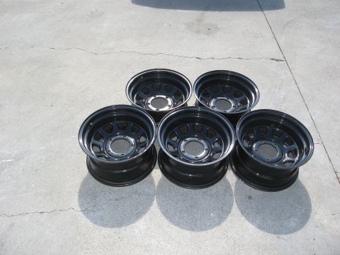 1986 Ford Bronco - Set of five black steel wheels with chrome trim rings, photographed on concrete.