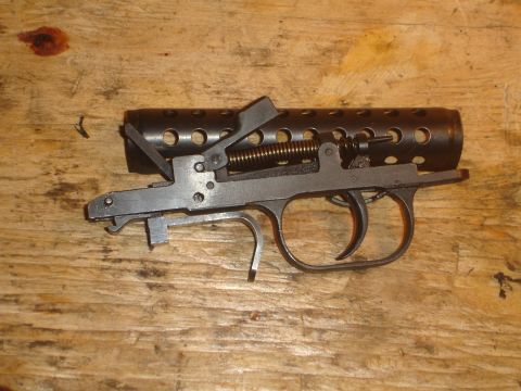 1989 Ford Bronco - Close-up of a firearm trigger assembly, including a perforated barrel shroud, resting on a wooden surface.