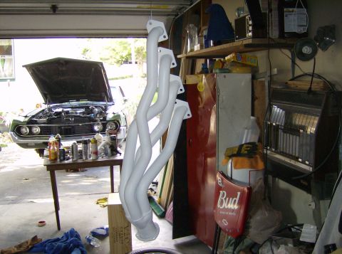 1970 Ford Ranchero - A set of white exhaust headers are displayed in a garage, with a car's engine bay visible.