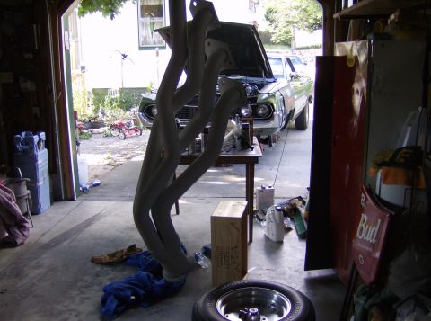 1970 Ford Ranchero - Exhaust headers are in the foreground of a garage scene with a green 1968 Ford Ranchero.