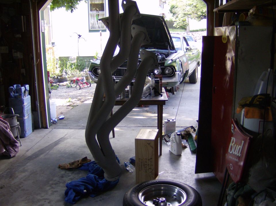 Ceramic-coated long-tube headers hanging in a garage doorway with a green muscle car outside