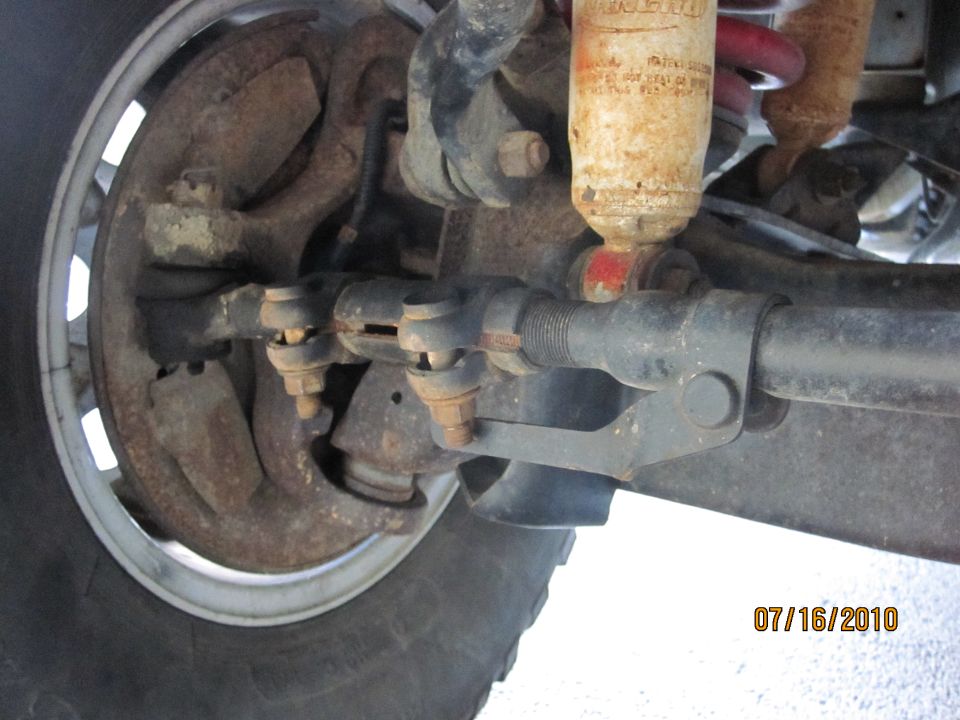 Close-up of rusty front suspension and steering linkage with a shock absorber and tire visible