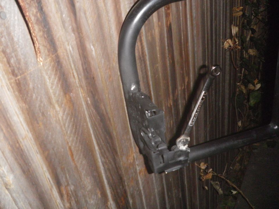 Part of a black metal frame with a wrench attached to it, against a corrugated metal background