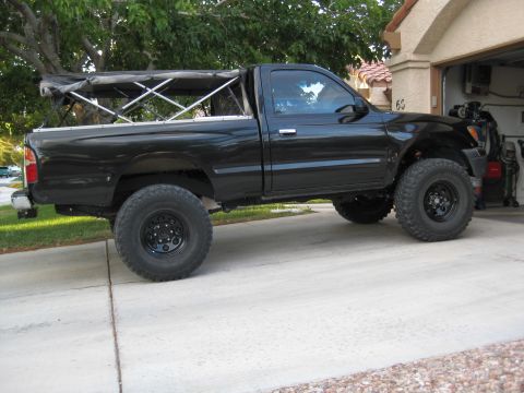2000 Toyota Tacoma - A black pickup truck is parked in a driveway with a tent frame in the bed.
