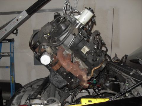 2007 Ford Mustang - An engine is suspended by a chain hoist, undergoing removal or installation within a vehicle's engine bay.