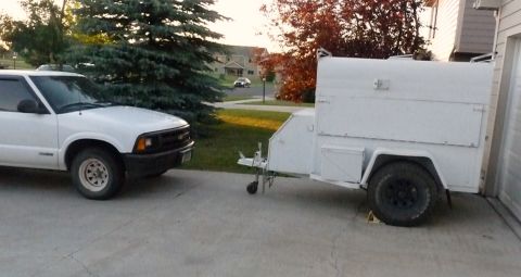 2006 Ford E350 - A white pickup truck is parked next to a white utility trailer in a driveway.
