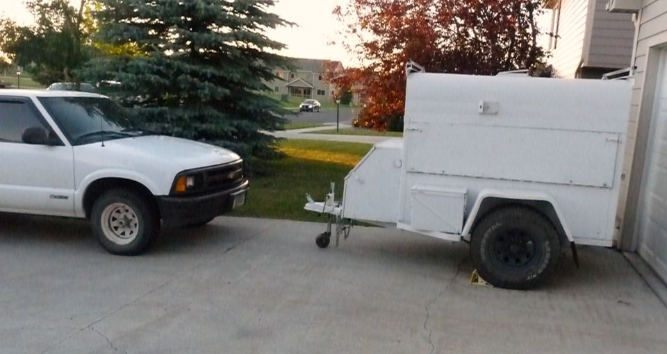 White pickup truck, front quarter view, parked next to a white utility trailer