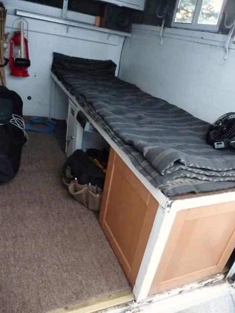 2006 Ford E350 - The interior of a camper van features a bed, storage, and a red lantern mounted on the wall.