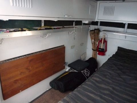 2006 Ford E350 - The interior of a camper van shows a bed, a wooden table, and storage compartments.