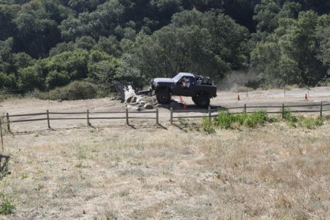1989 Ford Bronco - A modified SUV navigates a challenging obstacle on a dirt track, kicking up dust.