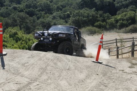 1989 Ford Bronco - A heavily modified truck navigates an off-road course, raising dust as it turns.