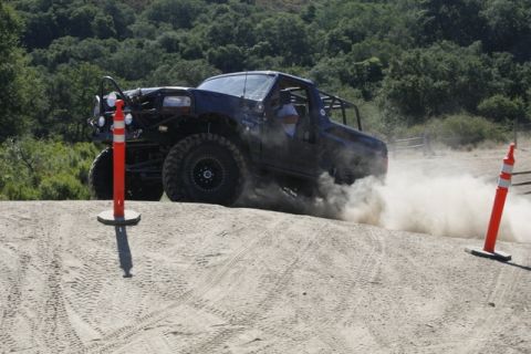 1989 Ford Bronco - A heavily modified truck navigates a dusty off-road course with orange traffic cones.
