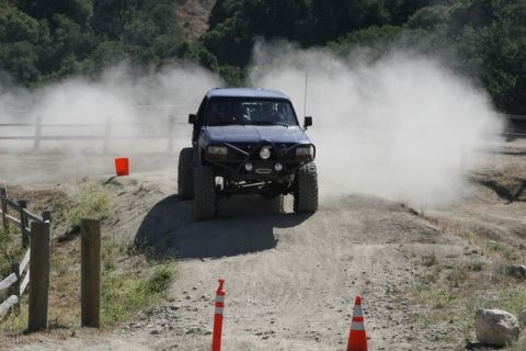 1989 Ford Bronco - This modified truck is navigating a dusty off-road course with a custom bumper and large tires.