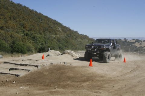 1989 Ford Bronco - A modified black truck navigates a dusty off-road course marked by orange cones.