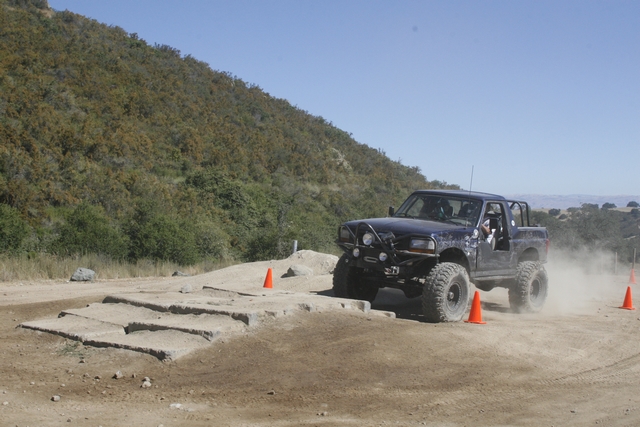 Dark blue off-road truck kicking up dust on a dirt course with orange cones