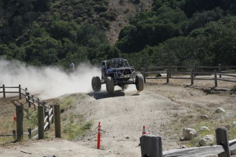 1989 Ford Bronco - A custom off-road buggy navigates a dusty track with a person watching in the background.