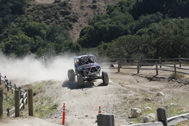 Off-road buggy kicking up dust on a dirt track, with a roll cage and large tires