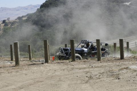 1989 Ford Bronco - An off-road buggy navigates a dusty course marked by wooden posts, with hills in the background.