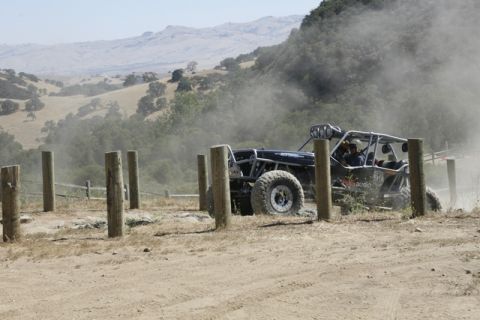 1989 Ford Bronco - An off-road buggy kicks up dust while navigating a course with wooden posts.