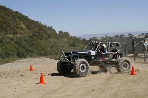 1989 Ford Bronco - A custom-built off-road buggy navigates a dusty course with spectators watching from a fence line.