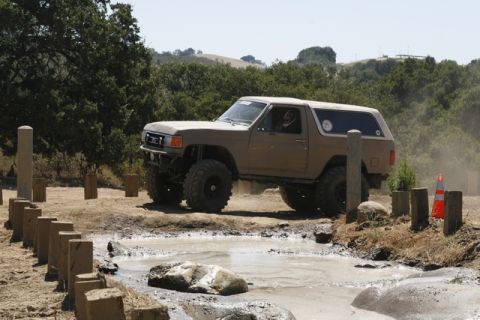 1989 Ford Bronco - This modified SUV is tackling a challenging off-road course with mud and obstacles.