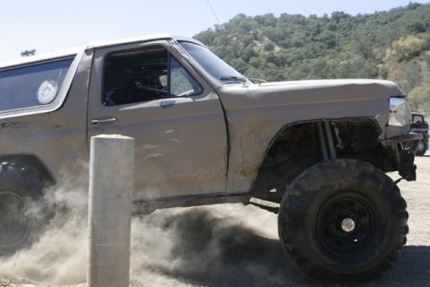 1989 Ford Bronco - This heavily modified SUV, likely from the 1980s, is shown in action, kicking up a cloud of dust during an off-road event.