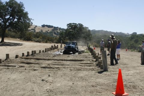 1989 Ford Bronco - A blue Jeep Wrangler navigates a challenging off-road course with onlookers observing the event.