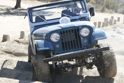 1989 Ford Bronco - A blue Jeep CJ-5 navigates an off-road obstacle course with a driver in a helmet.