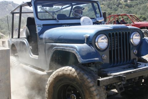 1989 Ford Bronco - A blue Jeep CJ-5 navigates an off-road trail, with a red vehicle visible in the background.