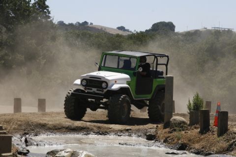 1989 Ford Bronco - Off-road vehicle navigates a muddy course kicking up dust.