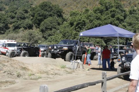 1989 Ford Bronco - A group of off-road vehicles and people are gathered outdoors, with some vehicles parked under a blue canopy.