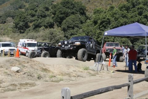 1989 Ford Bronco - Multiple off-road vehicles, including a black pickup and a red truck, are gathered at an outdoor event.